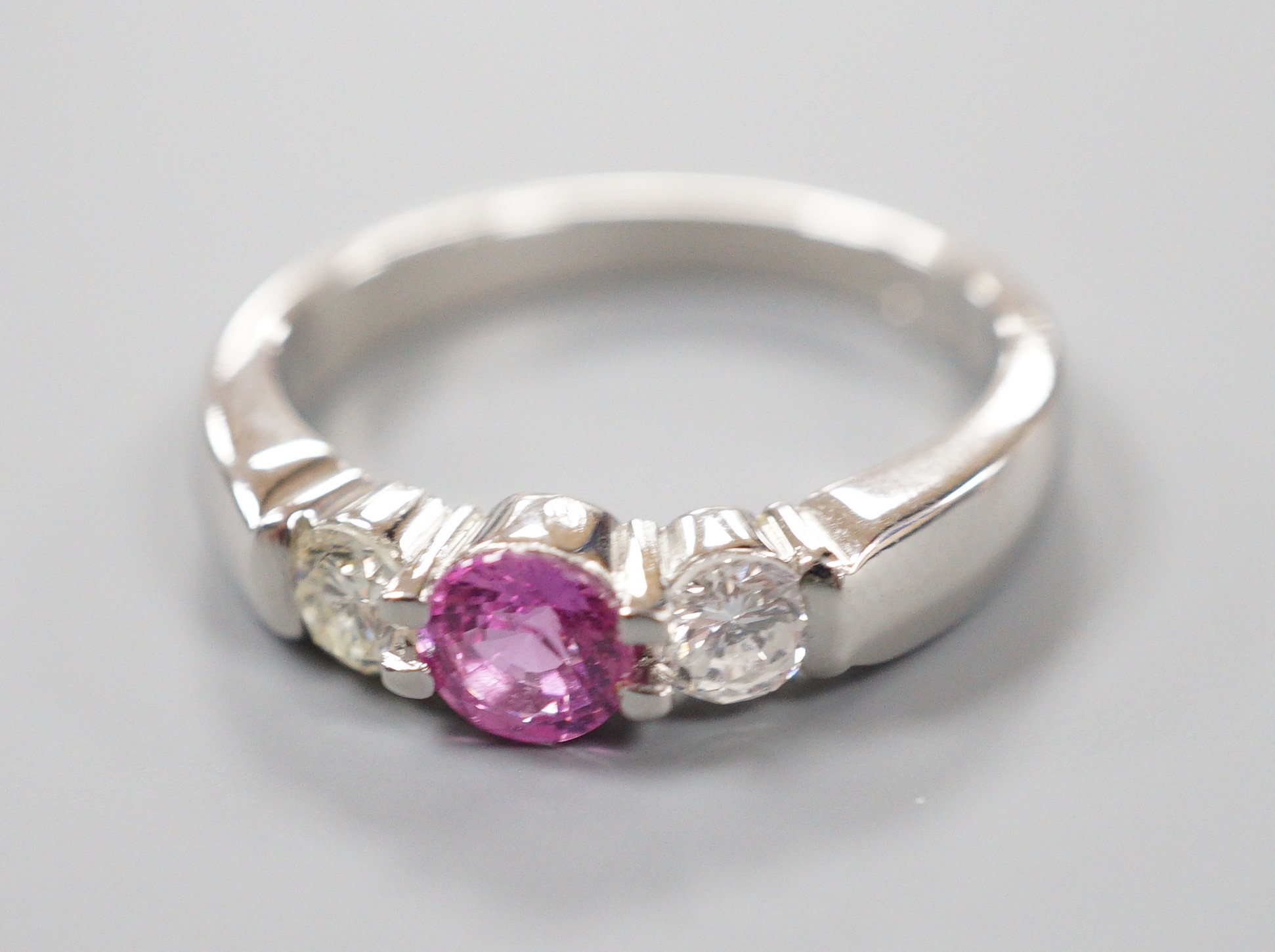 A modern platinum, single stone pink sapphire and two stone diamond set ring, size M/N, gross weight 6.5 grams